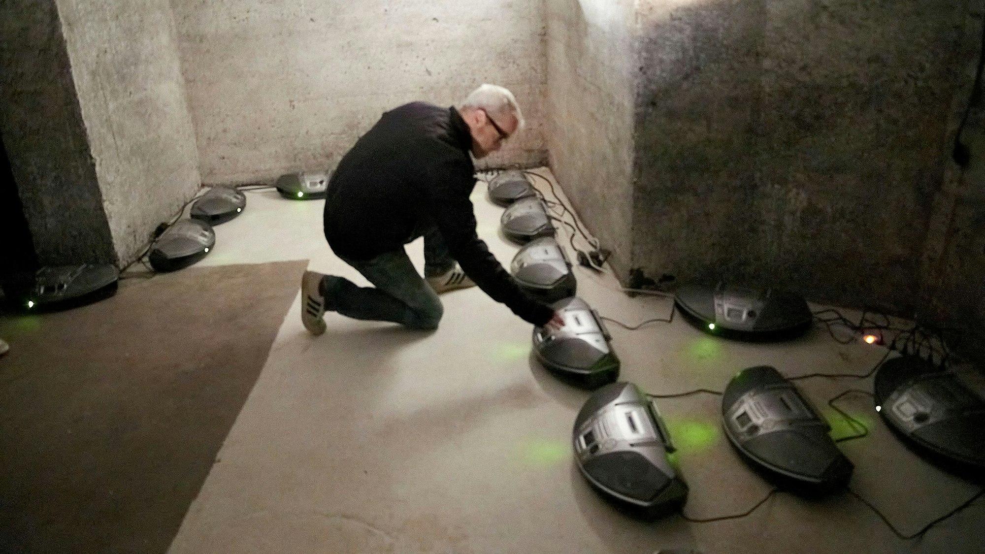 Mark Polscher kniet vor einem von insgesamt 24 CD-Spielern, die auf dem Boden eines Luftschutzraums stehen.