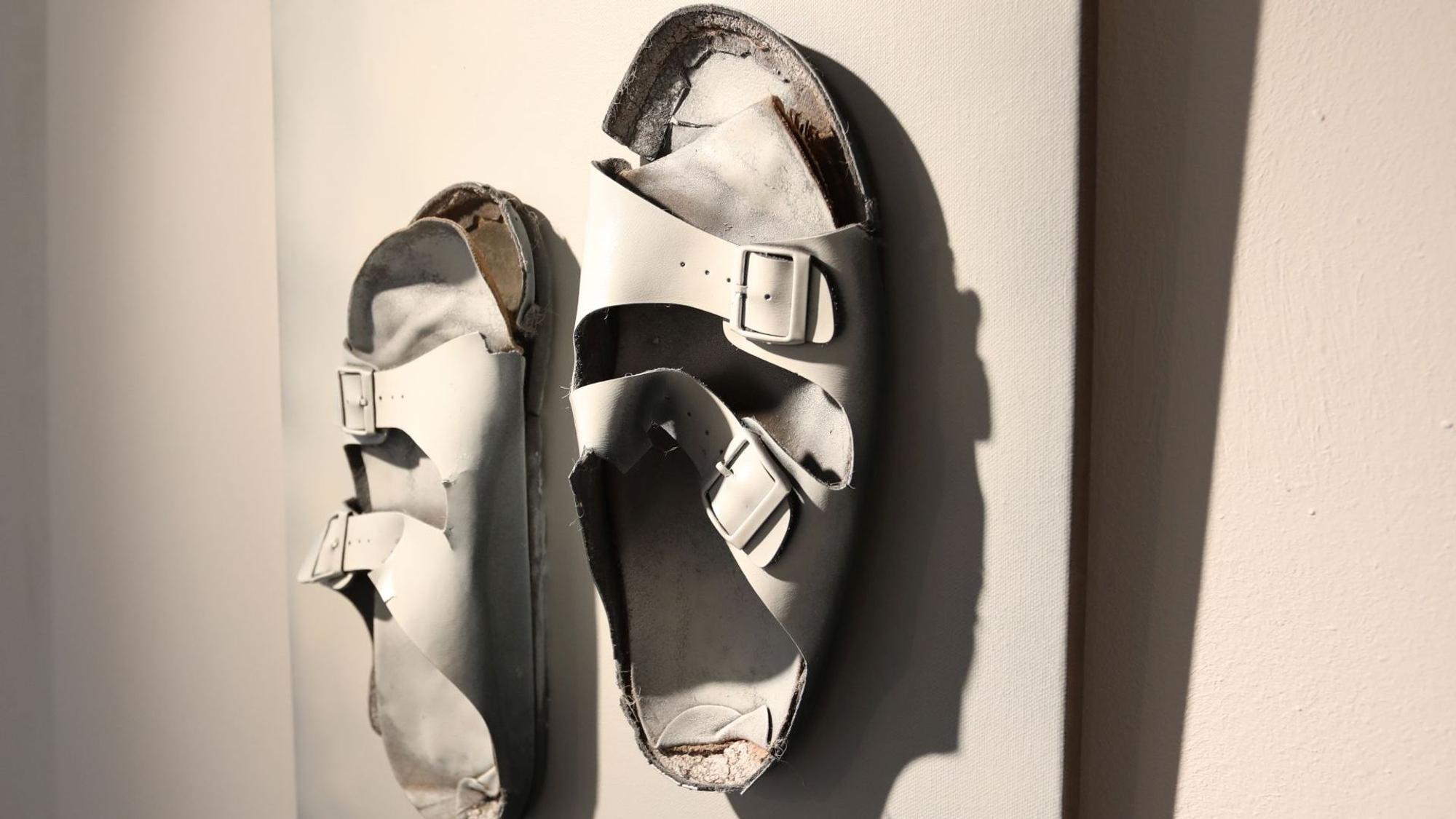 Zwei ausgetretene weiße Sandalen bilden eine Skulptur.
