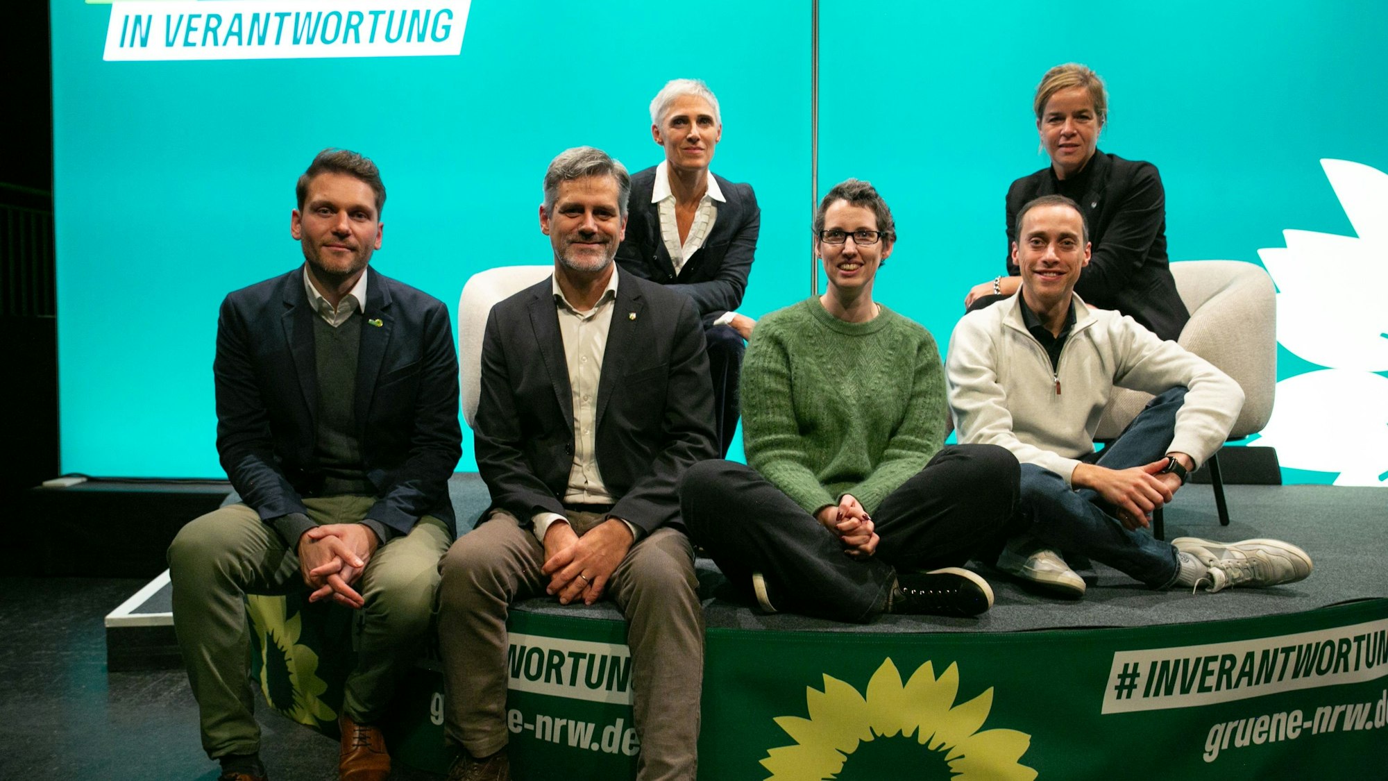 Drei Frauen und drei Männer posieren auf einem Podium.