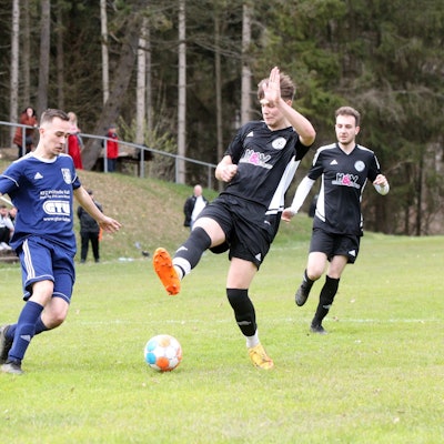 Maurice Gölden versucht sich den Ball am mit gestrecktem Bein heraneilendem Stotzheimer Spieler vorbeizulegen.
