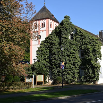 Das efeubewachsene Gebäude der Alte Kaplanei in Odenthal. Dahinter der Kirchturm von St. Pankratius.