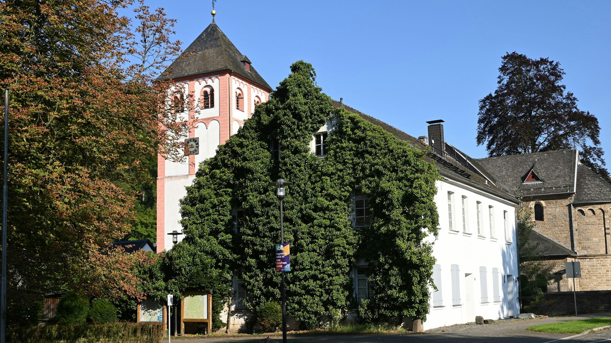 Ein efeubewachsenes Haus, dahinter eine Kirche.