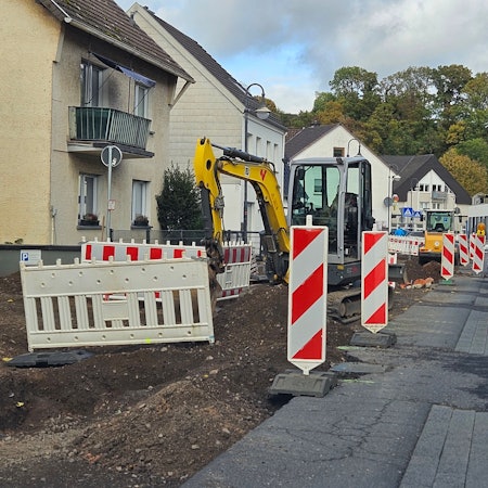 Zu sehen ist eine von Baggern aufgerissene Straßenhälfte, die mit Warnbaken abgesperrt ist, und eine Seite, auf der Autos fahren.
