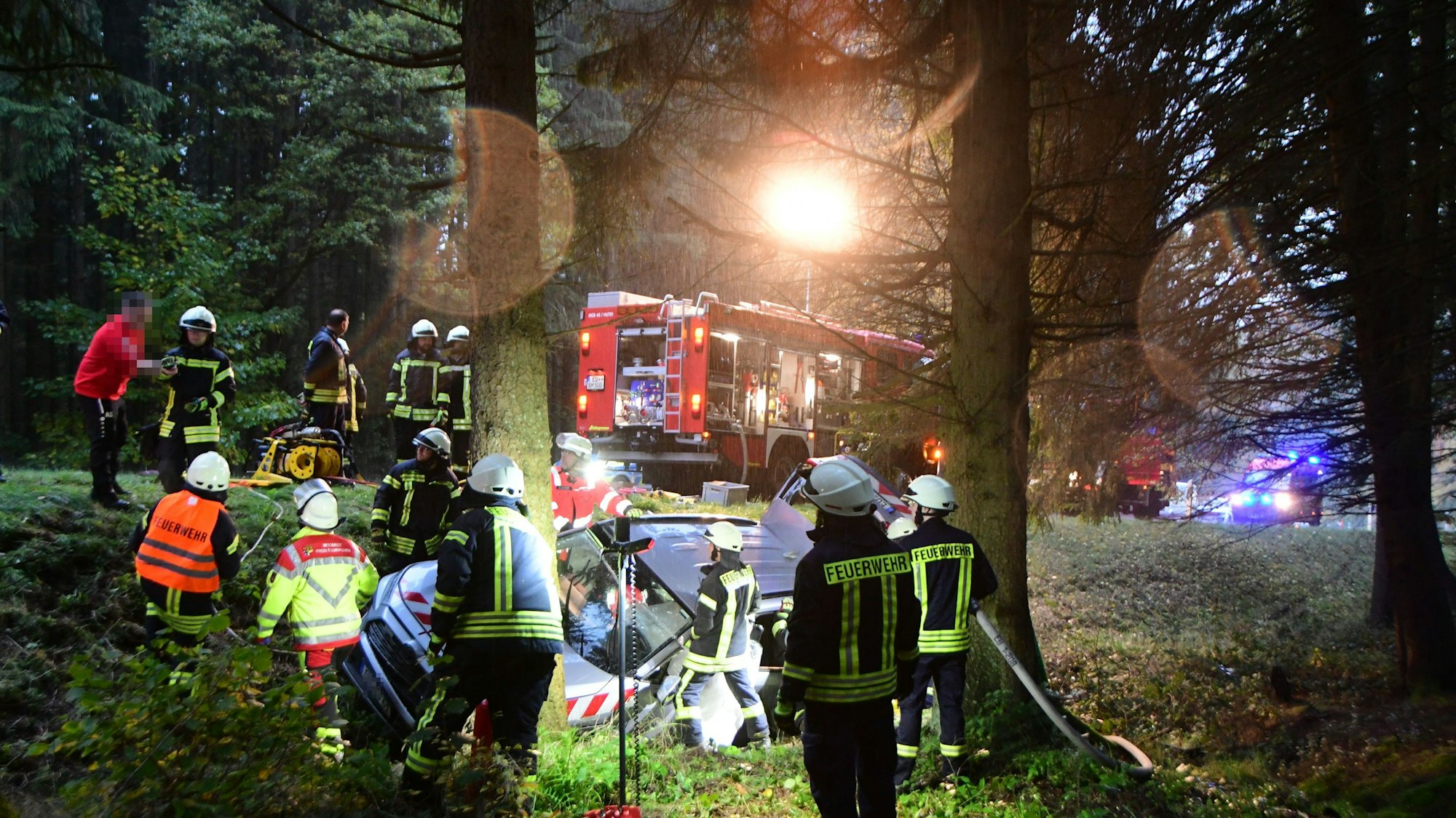 Das Bild zeigt die Feuerwehr bei der Arbeit. Sie befreit den Mann aus seinem Auto.