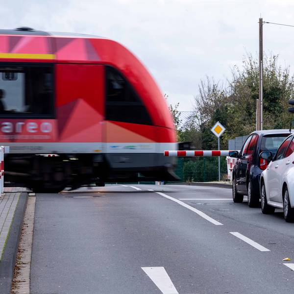 Das Bild zeigt einen Zug, der einen Bahnübergang passiert. Autos stehen vor der geschlossenen Schranke.