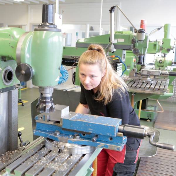 Eine junge Frau stellt eine Fräsmaschine ein.