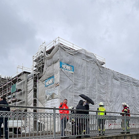 Mehrere Menschen stehen auf einer Brücke vor dem mit einem Gerüst umbauten Johannes-Sturmius-Gymnasium in Schleiden.