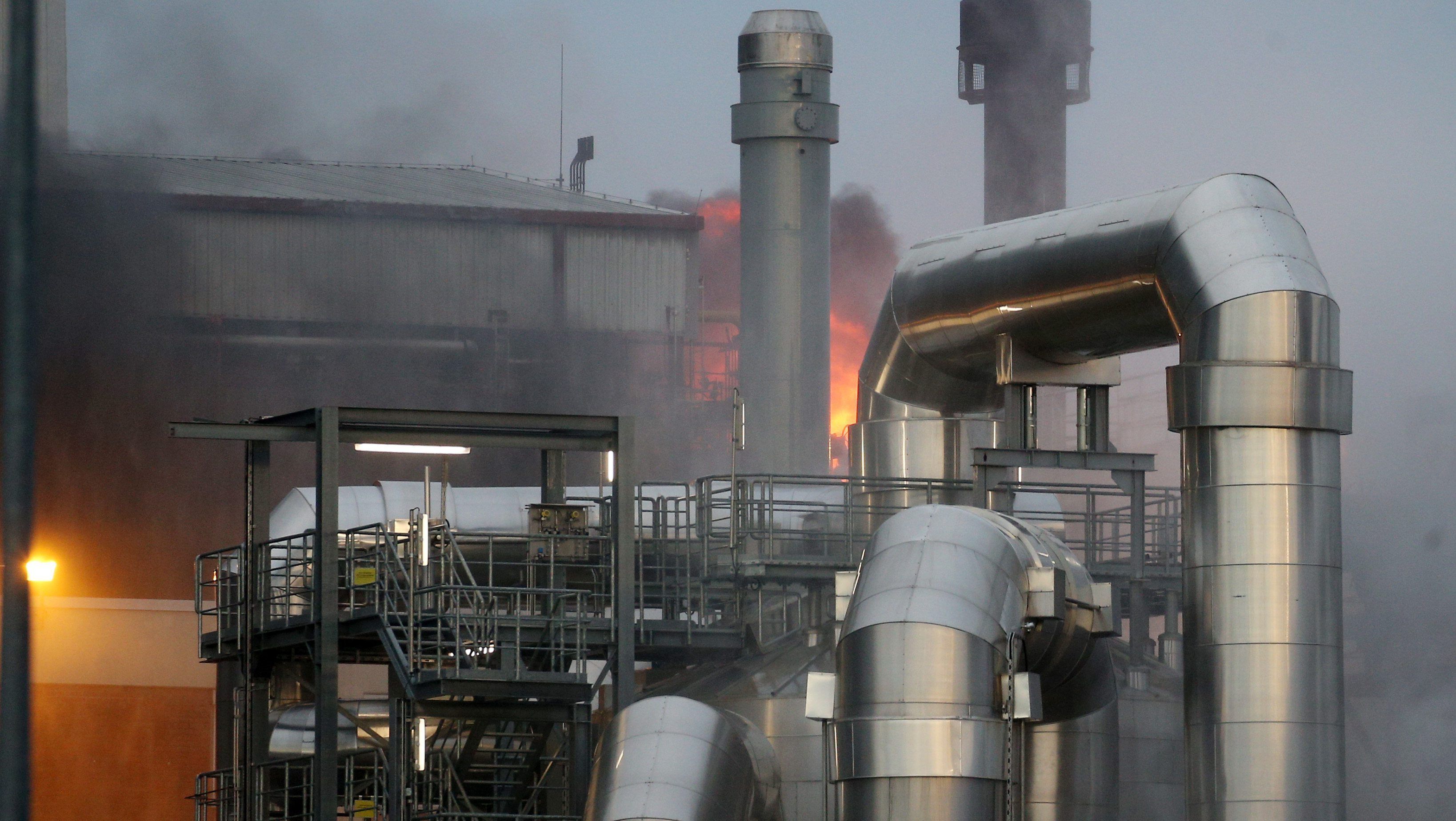 Auf einem Industriegelände ist dichter, dunkler Rauch zu sehen - im Hintergrund ist eine große Flamme erkennbar.