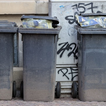 Mehrere volle Mülltonnen für Restmüll stehen an einer Hauswand.