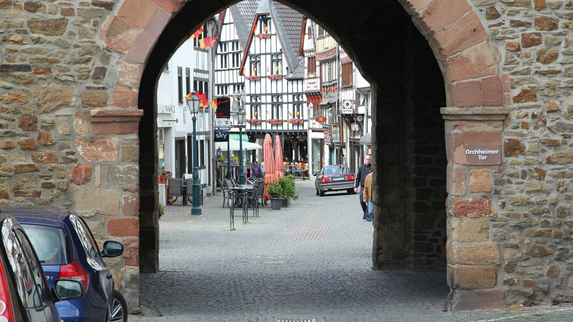 Die Innenstadt von Bad Münstereifel im Jahr 2013, durch das Orchheimer Tor fotografiert. Vor demTor parken Autos. Ein Wagen fährt im Hintergrund über die Orchheimer Straße.
