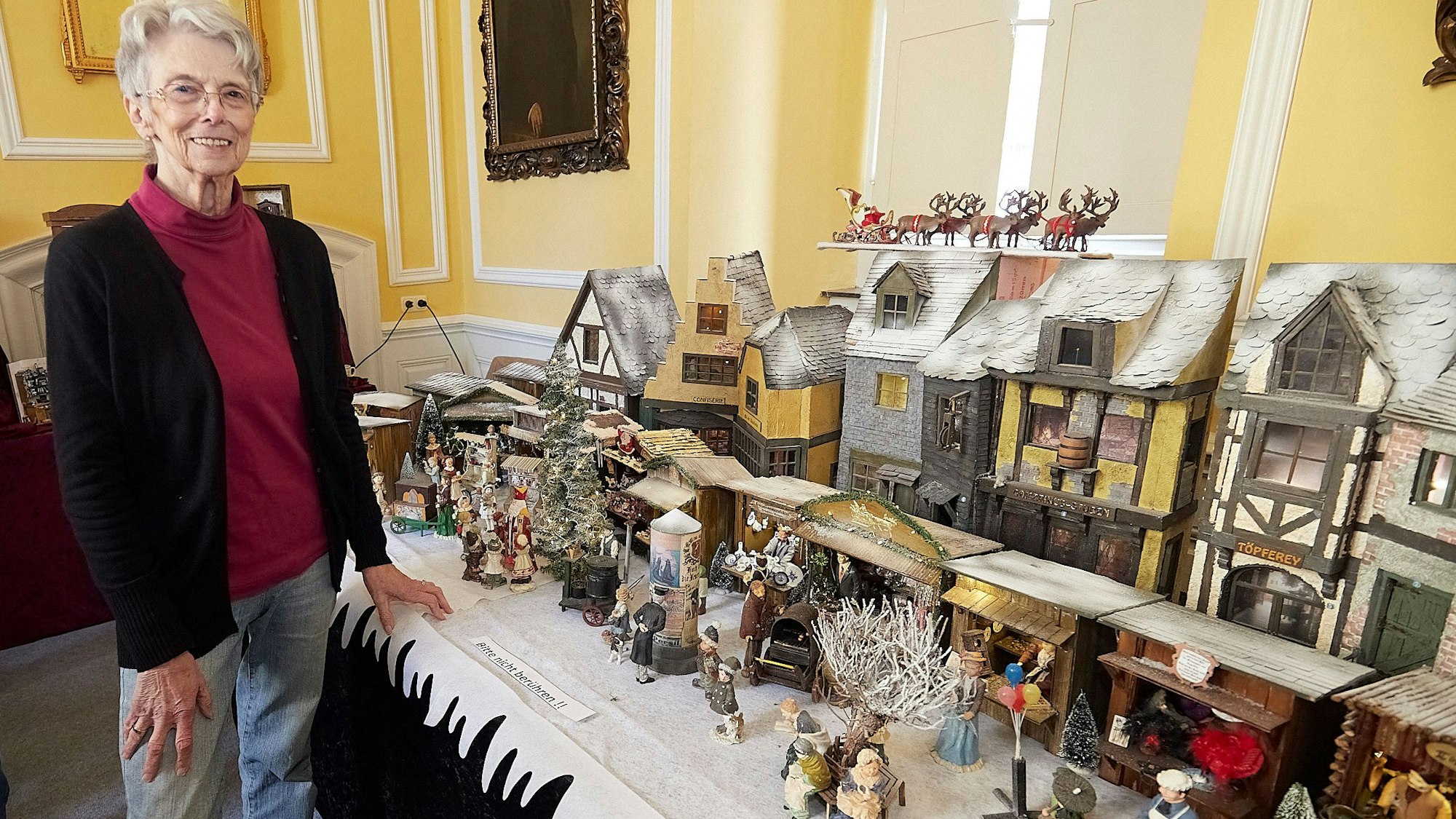 Die Ausstellerin vor dem Modell ihres Weihnachtsmarkts mit idyllischen Fachwerkhäuschen.