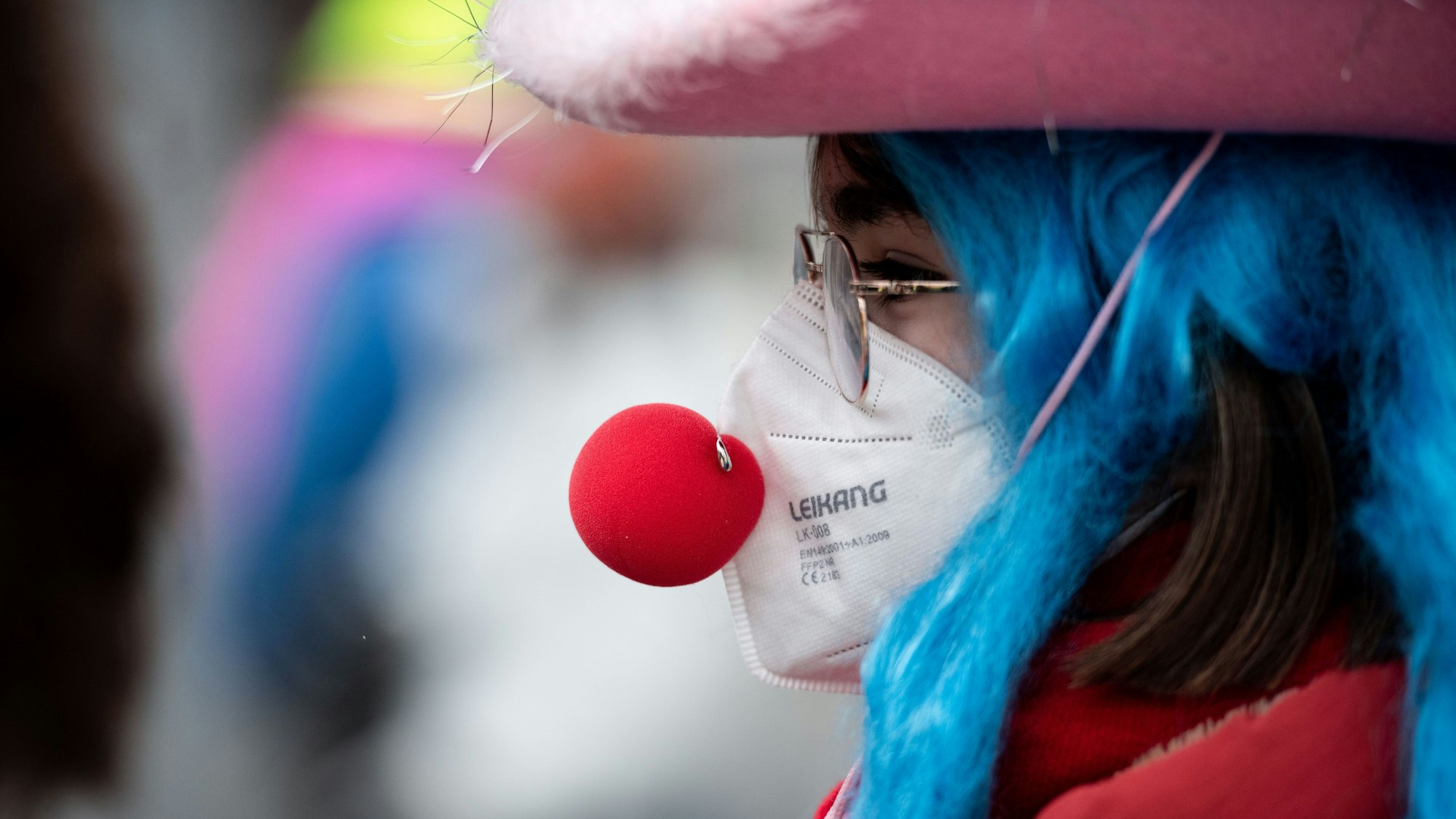 Eine verkleidete Frau trägt eine Clownsnase über einer FFP2-Maske.
