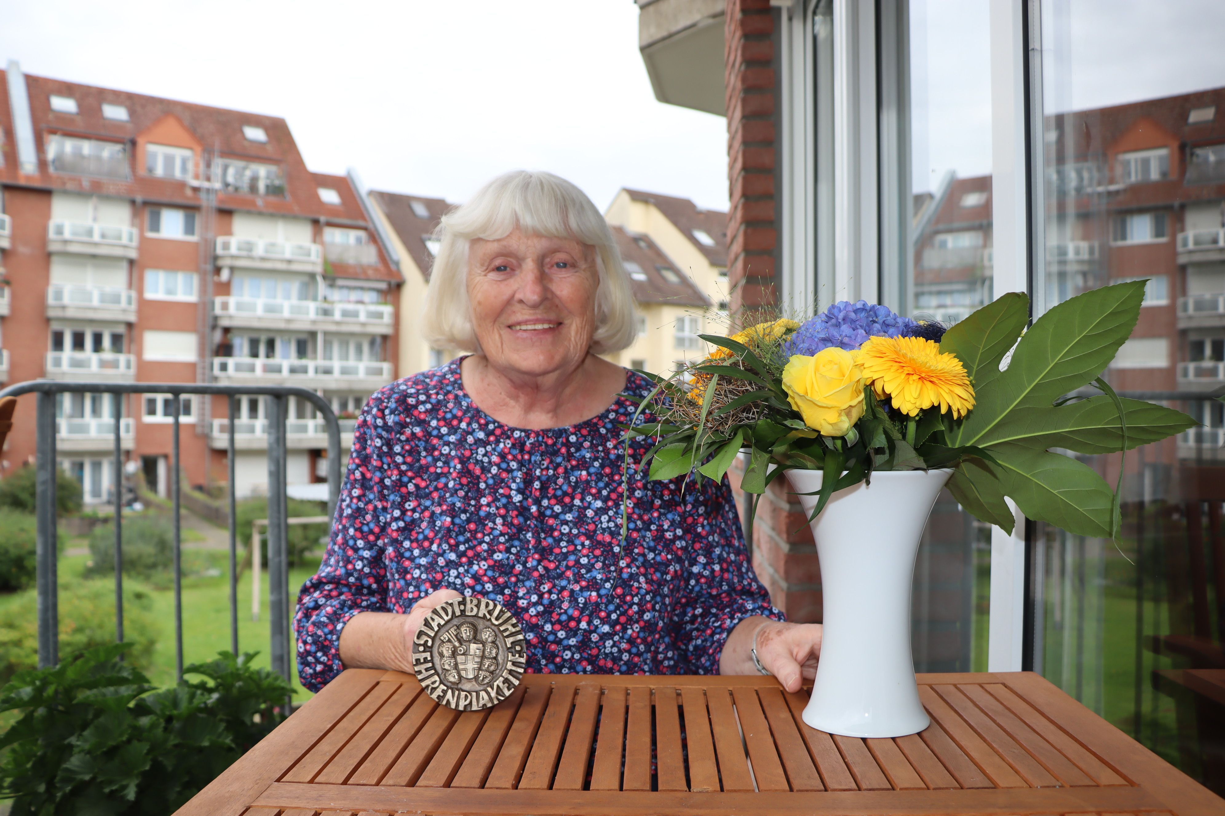 Eine Frau hält eine Plakette ins Bild, darauf steht "Stadt Brühl - Ehrenplakette".