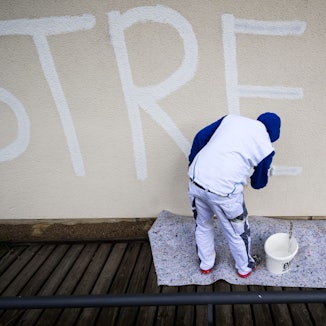 Ein Maler überdeckt am städtischen Nord-Ost-Bad einen schwarzen Schriftzug „Streik“ mit weißer Farbe, um anschließend die komplette Wand flächendeckend neu zu streichen. (Archivbild)