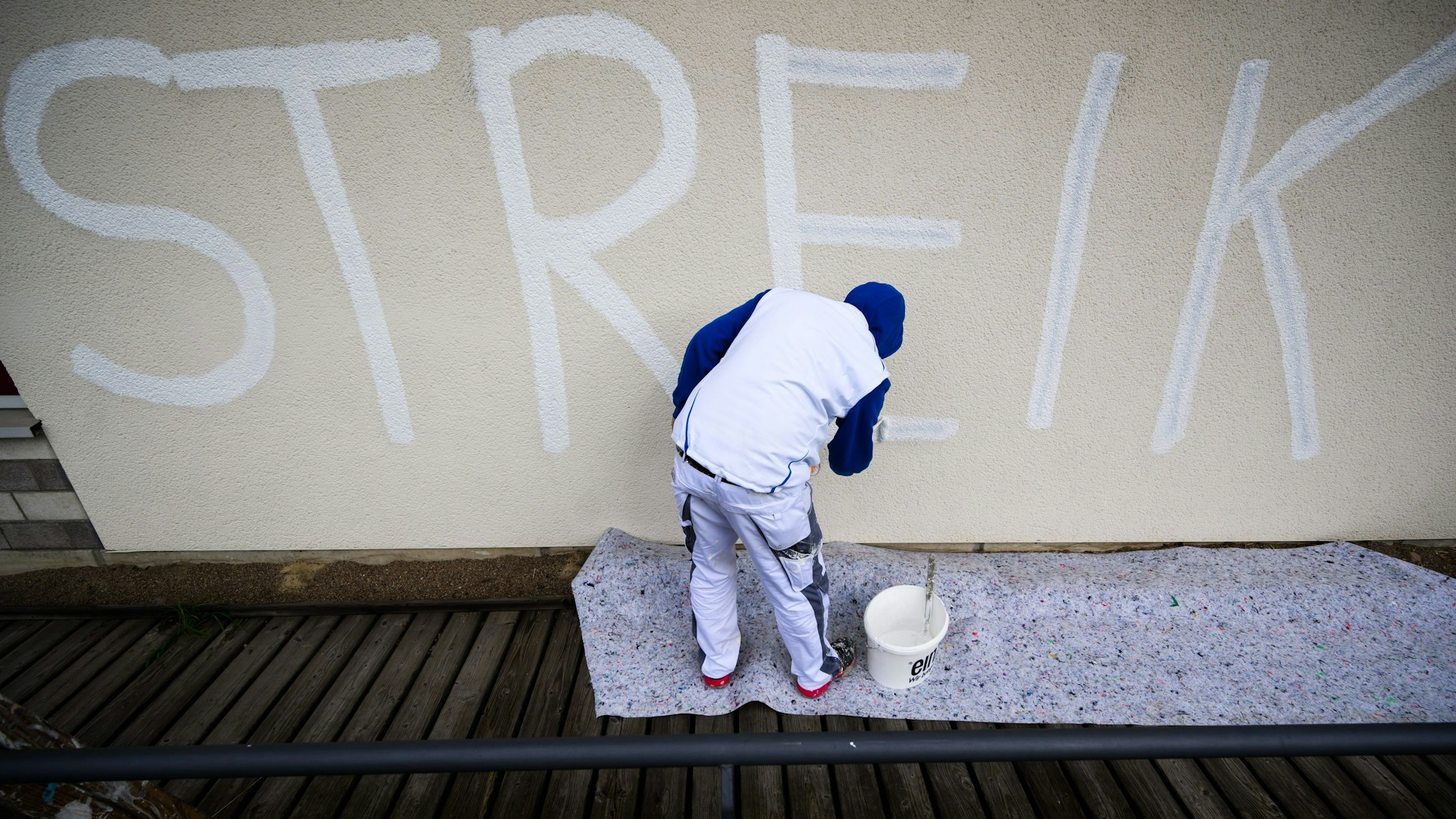 Ein Maler überdeckt am städtischen Nord-Ost-Bad einen schwarzen Schriftzug „Streik“ mit weißer Farbe, um anschließend die komplette Wand flächendeckend neu zu streichen. (Archivbild)