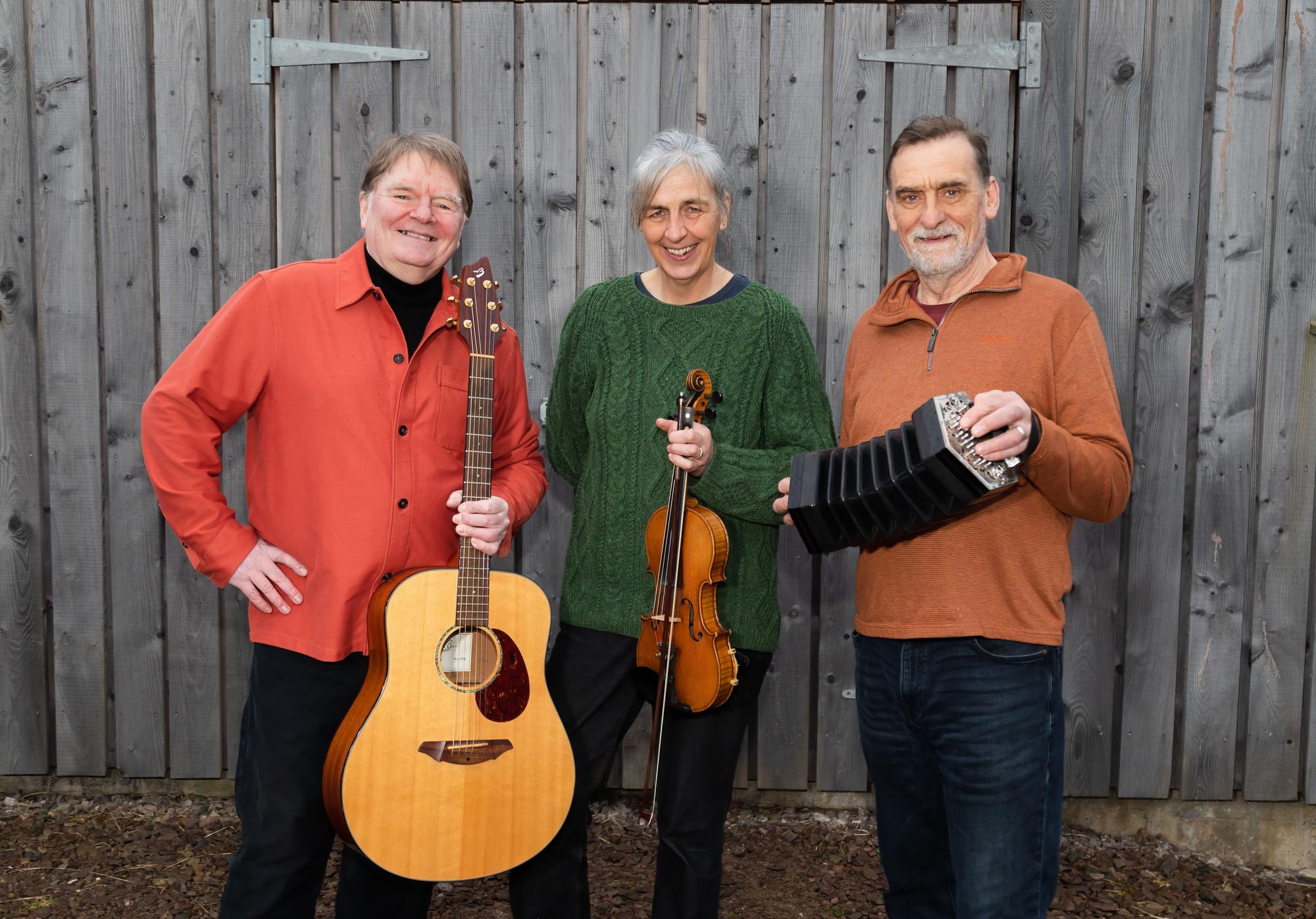 Die drei Musiker der Band Scaladal posieren vor einer Holzwand.