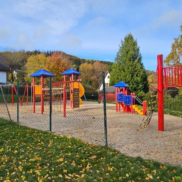 Zu sehen ist das Tor des Bolzplatzes und mehrere bunte Geräte des Spielplatzes.
