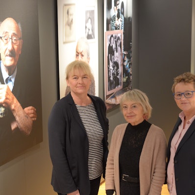 Dr. Heike  Lützenkirchen (l.) und Petra Goerge (r.) stellen im  Stadtmuseum Euskirchen mit Kuratorin Gisela Kayser die Sonderausstellung „Lonka Projekt“ vor. Sie stehen vor einer Reihe von Porträts von Holocaust-Überlebenden.