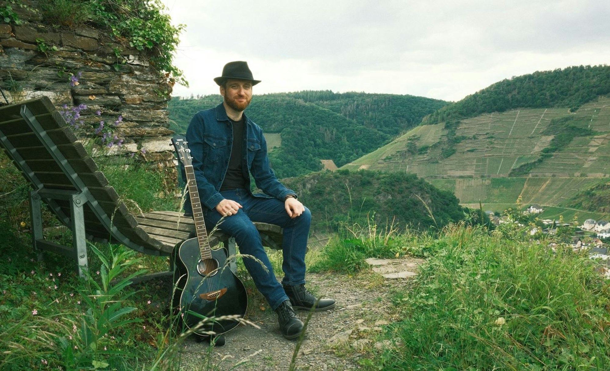 Cameron Arndt sitzt auf einer Bank, eine Gitarre lehnt neben ihm.