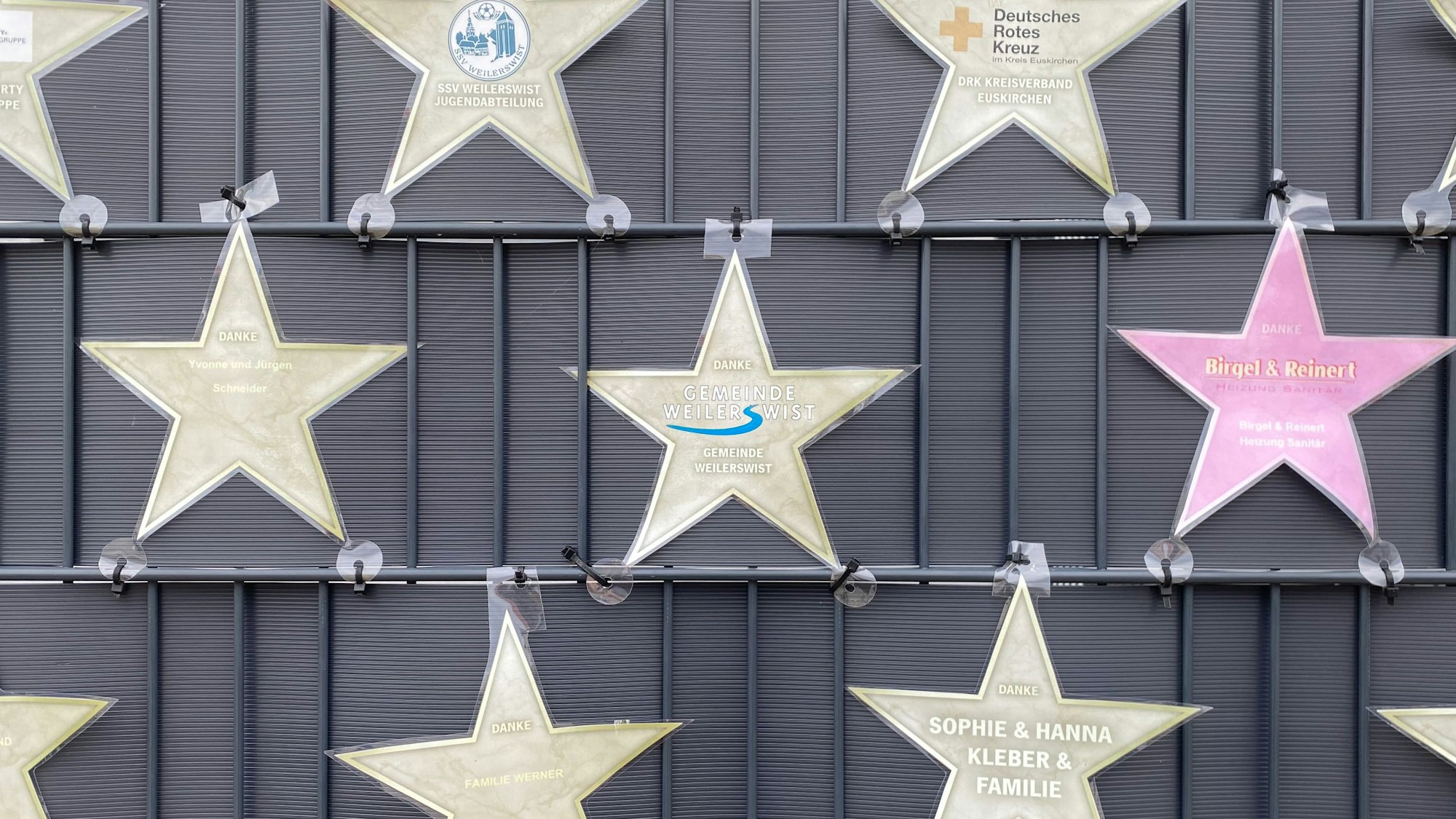 An einem Zaun hängen laminierte Sterne mit verschiedenen Namen.