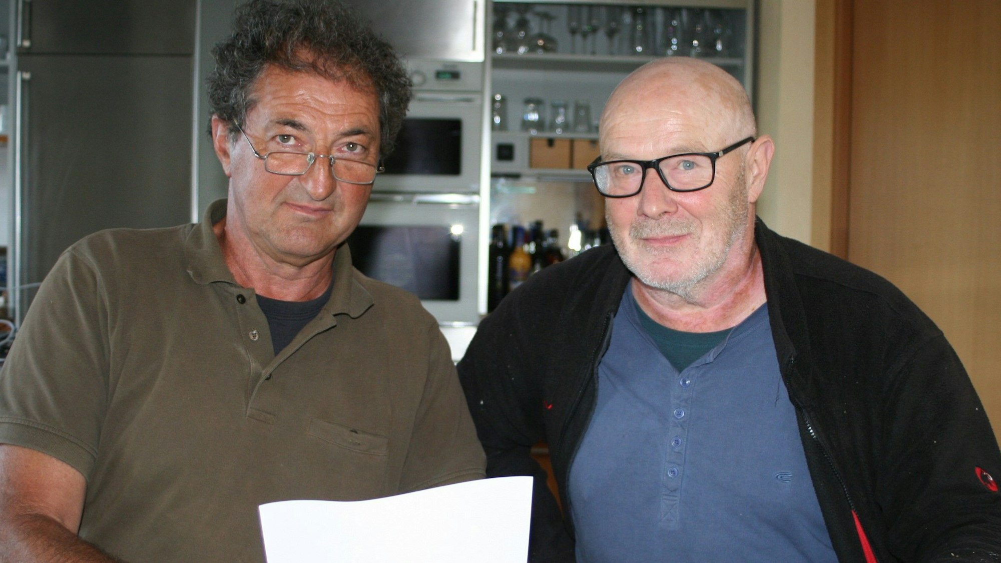 Zwei ältere Männer halten ein Blatt Papier.