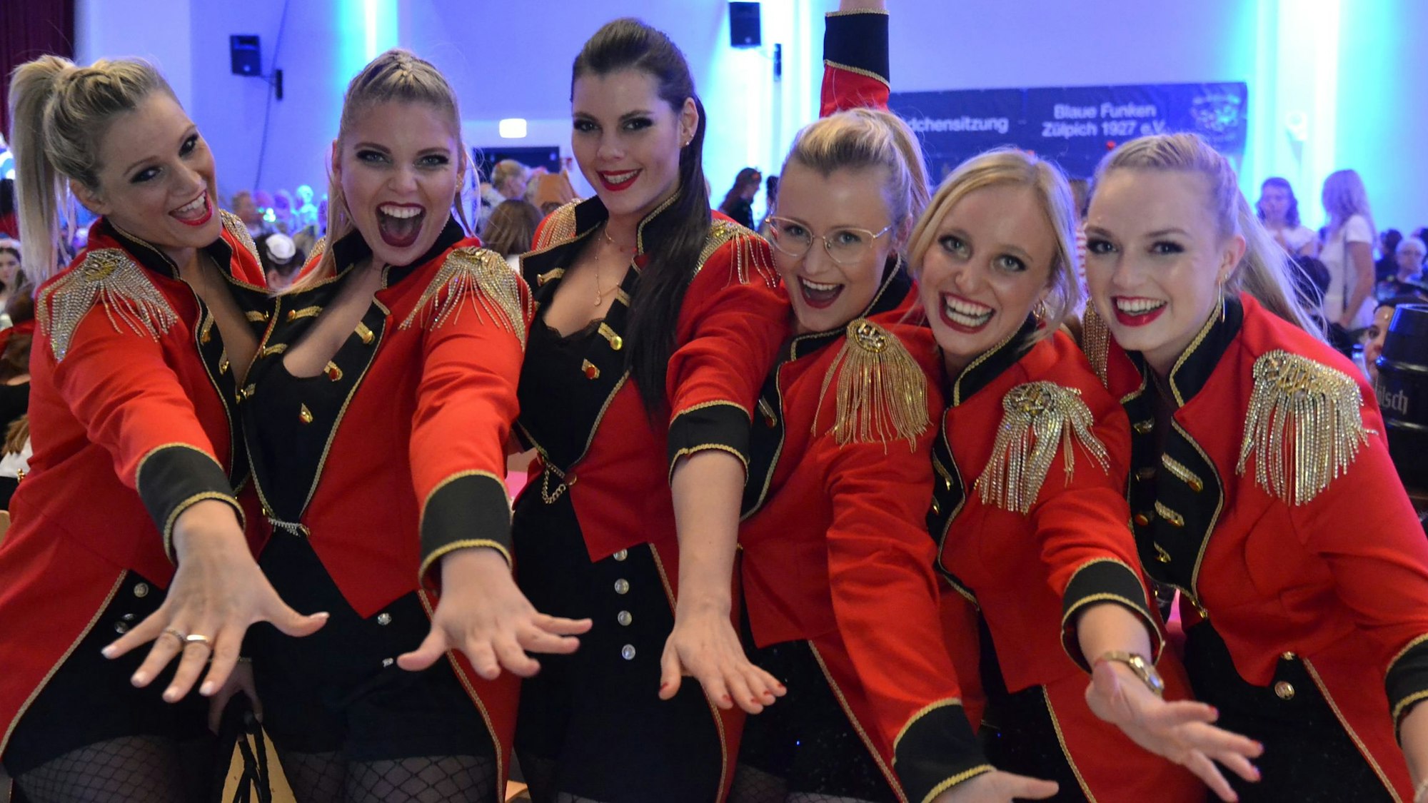 Das Bild zeigt sechs Frauen, die in roten Fracks für die Kamera posieren.