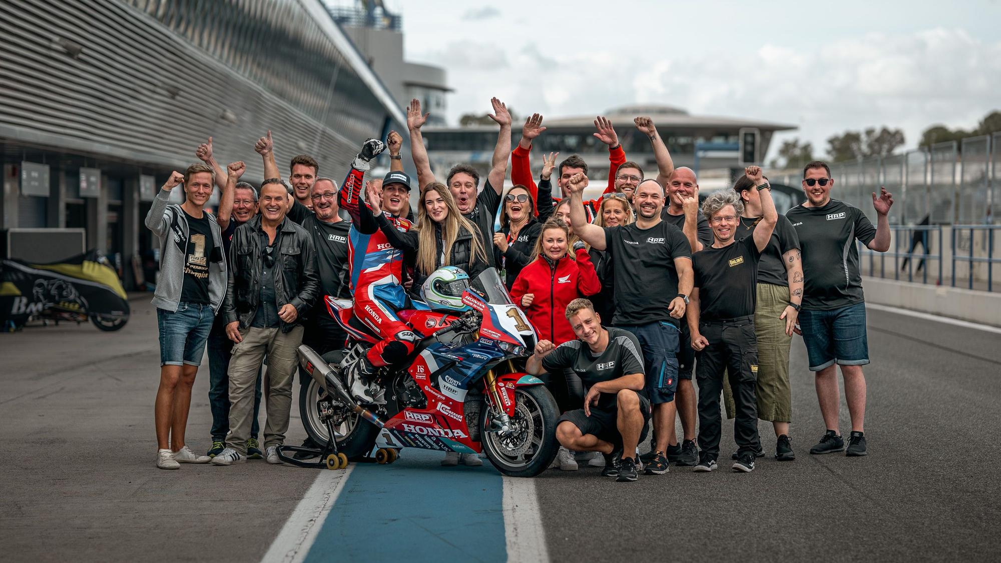 Eine Gruppe steht jubelnd auf einer Rennstrecke. In der Mitte von ihnen ist der oberbergischen Motorradrennfahrer Florian Alt auf seiner Honda.