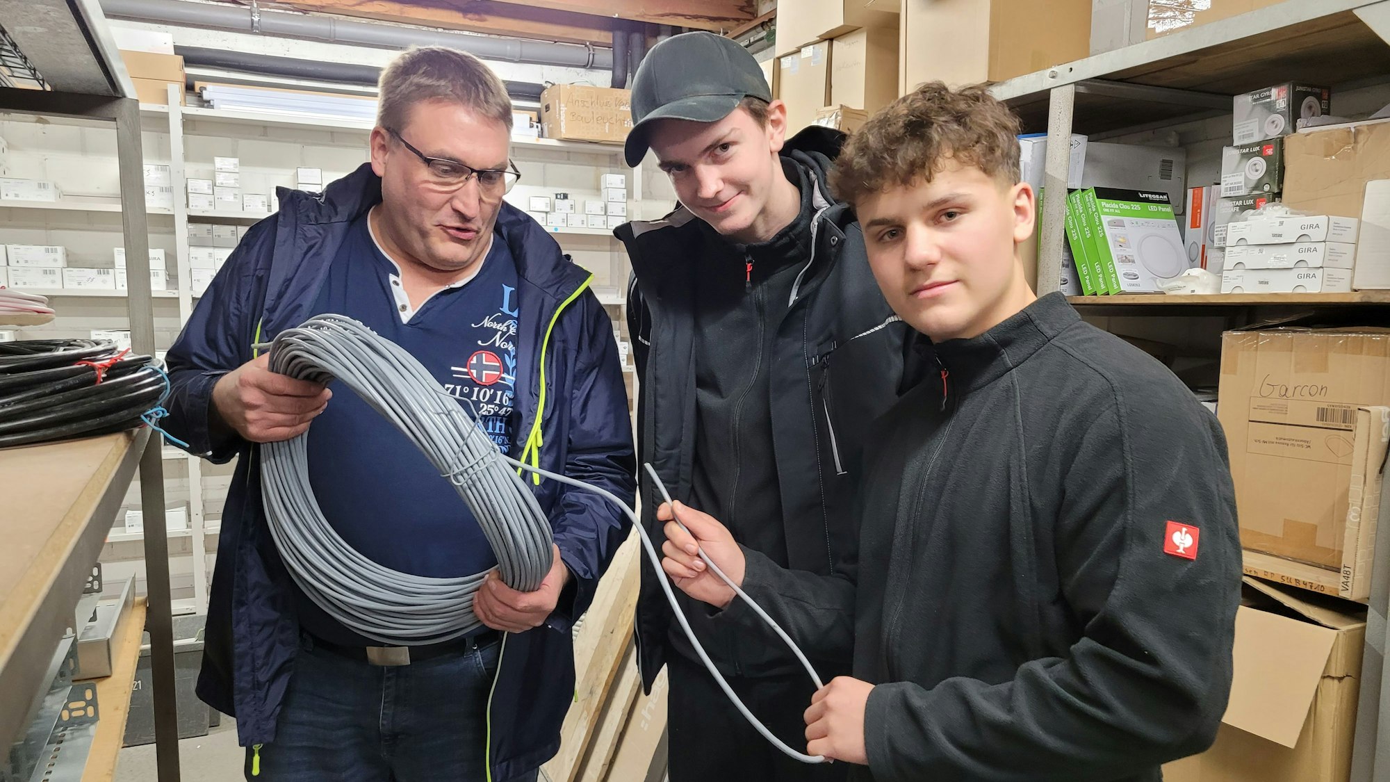 Zu sehen sind ein Erwachsener und zwei Jugendliche, die sich ein aufgerolltes meterlanges Kabel anschauen.