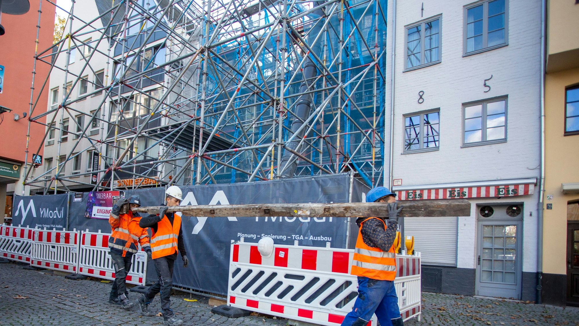 Arbeiter tragen einen Eichenbalken aus einer Baustelle.