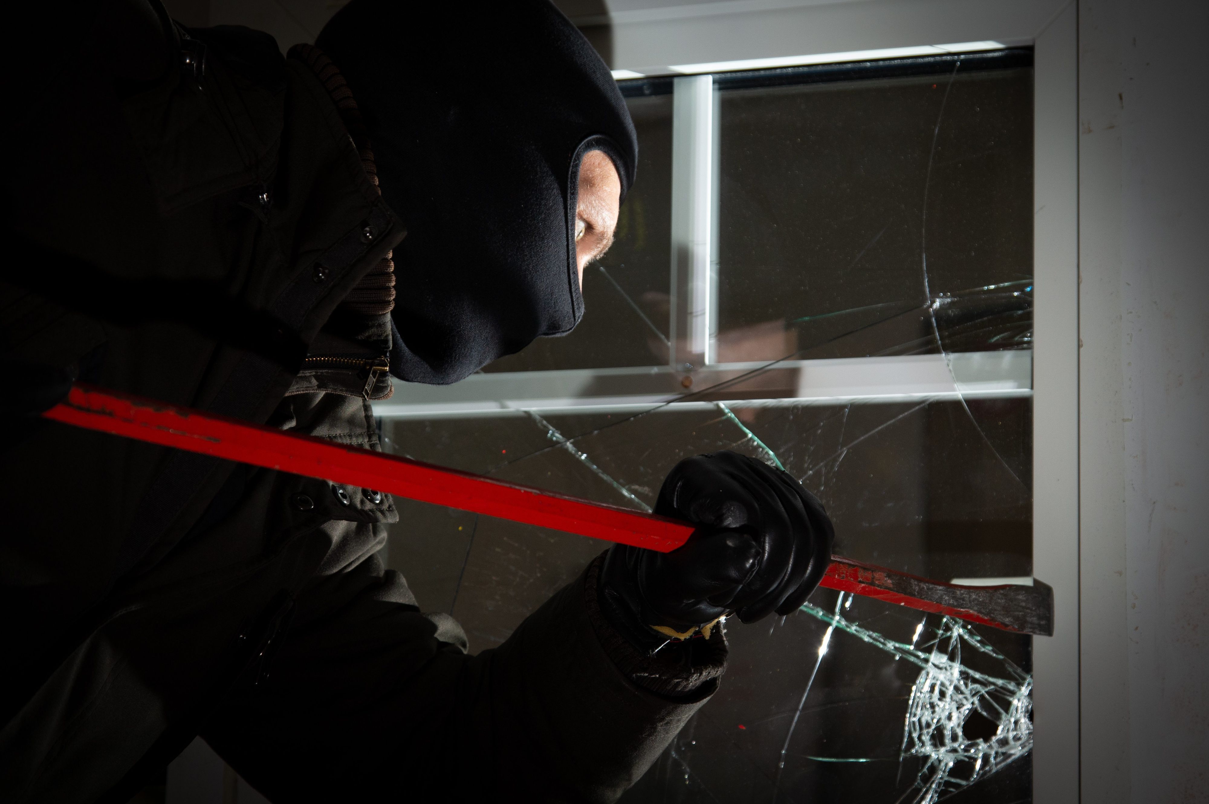 Ein als Einbrecher verkleideter Mann bricht mit einem Kuhfuß ein Fenster auf. In der dunklen Jahreszeit sind auch wieder mehr Einbrecher und Diebe unterwegs.