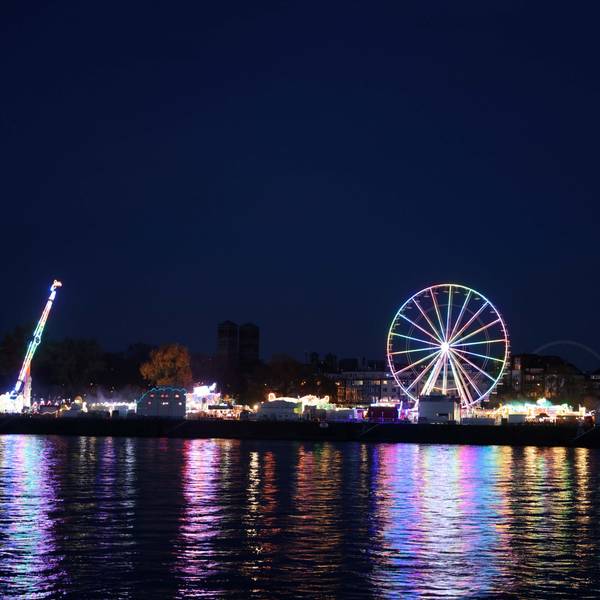 Ein beleuchtetes Riesenrad spiegelt sich im Rhein.