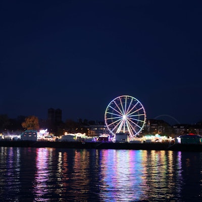 Ein beleuchtetes Riesenrad spiegelt sich im Rhein.