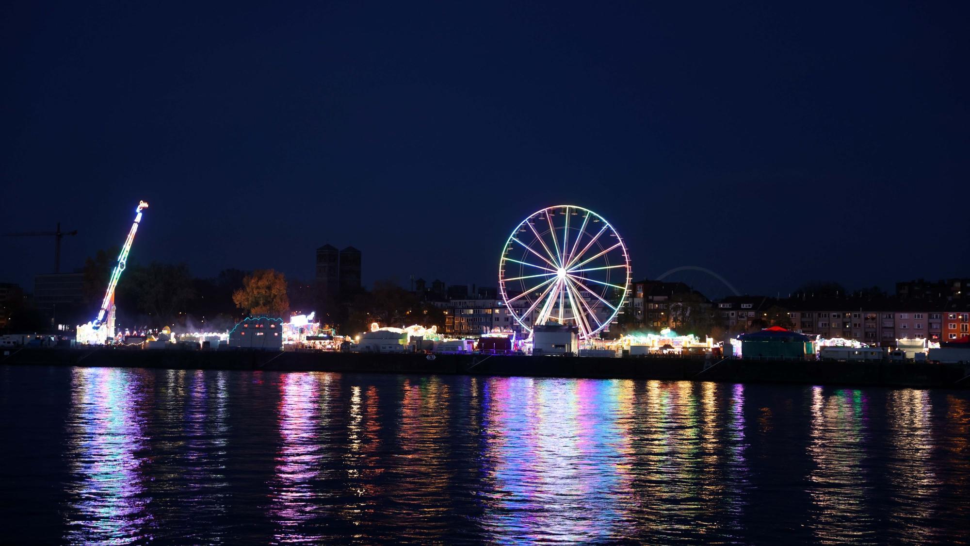 Die Lichter spiegeln sich im Rhein, von der linksrheinischen Seite aus gesehen. Kirmes