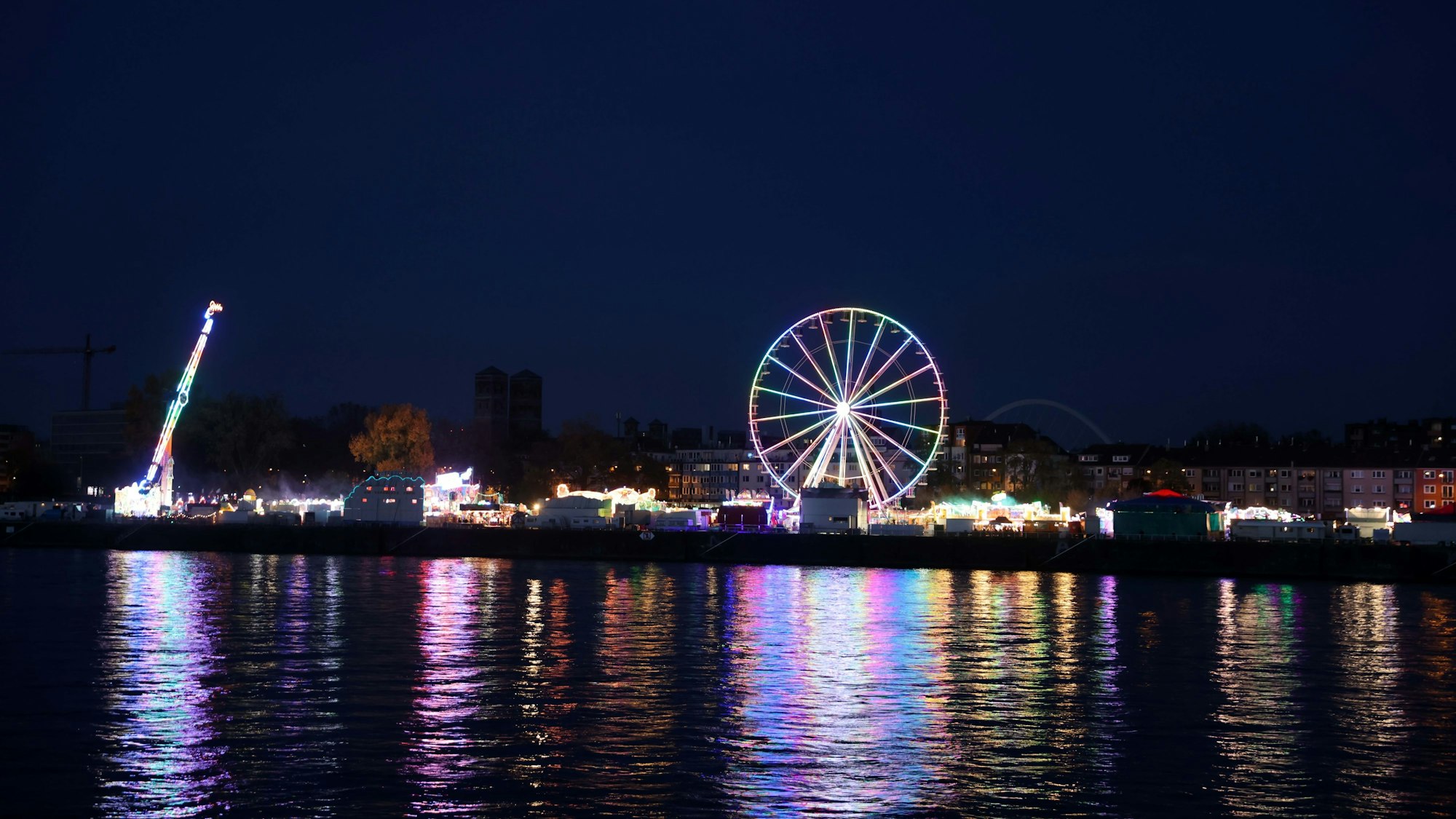 Die Lichter spiegeln sich im Rhein, von der linksrheinischen Seite aus gesehen. Kirmes