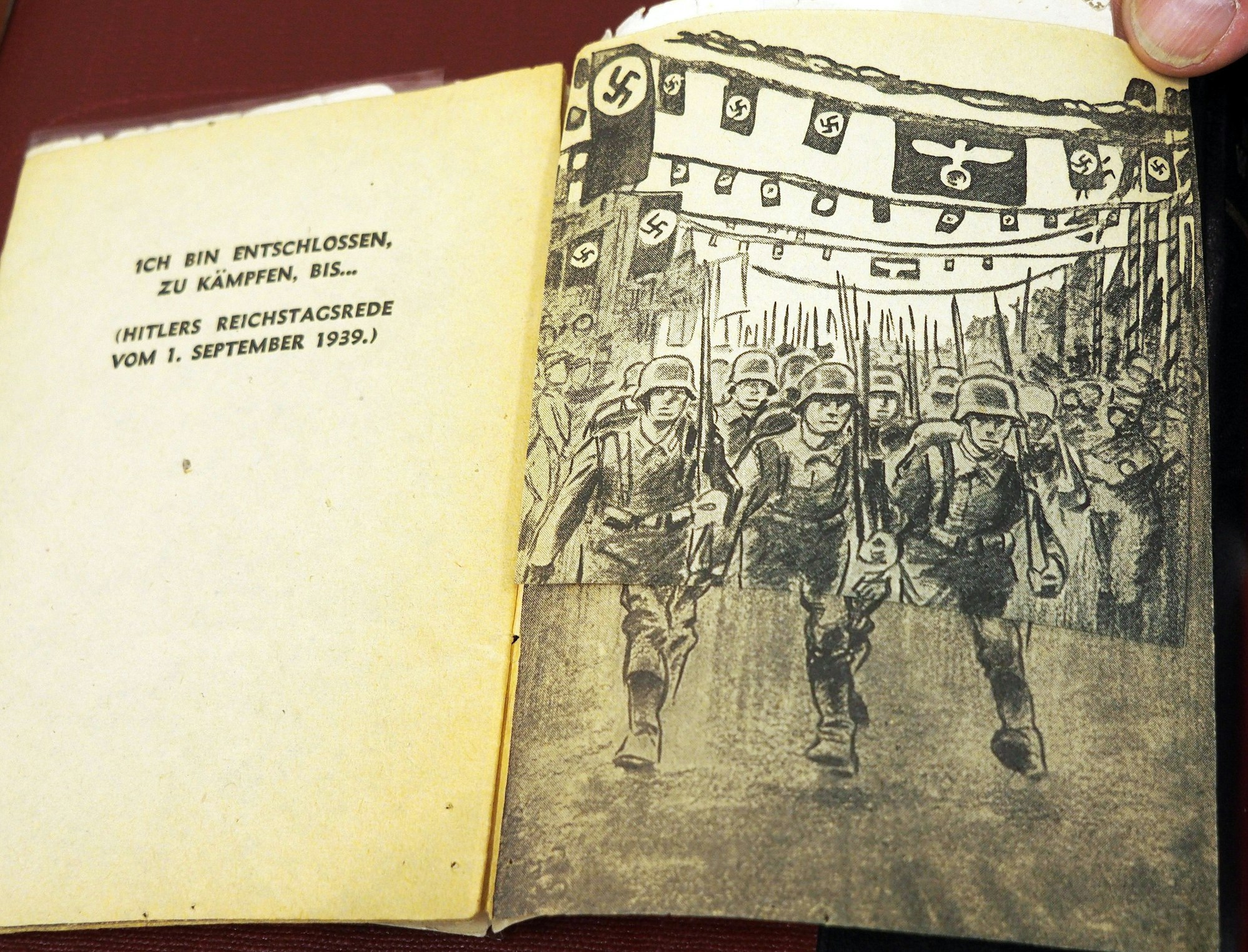 Soldaten, die mit entschlossenen Gesichtern und geschulterten Gewehren unter Hakenkreuzflaggen marschieren