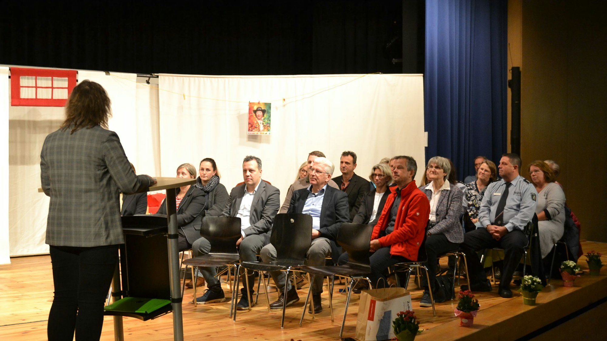 Rund 20 Teilnehmer der Auftaktveranstaltung sitzen in Reihen auf einer Bühne und hören einen Vortrag.