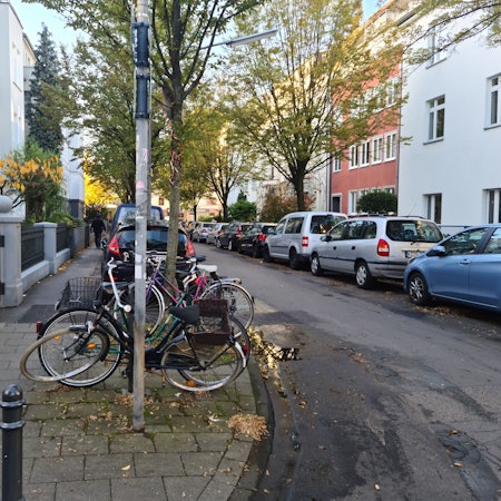Blick in eine Straße mit parkenden Autos und abgestellten Fahrrädern