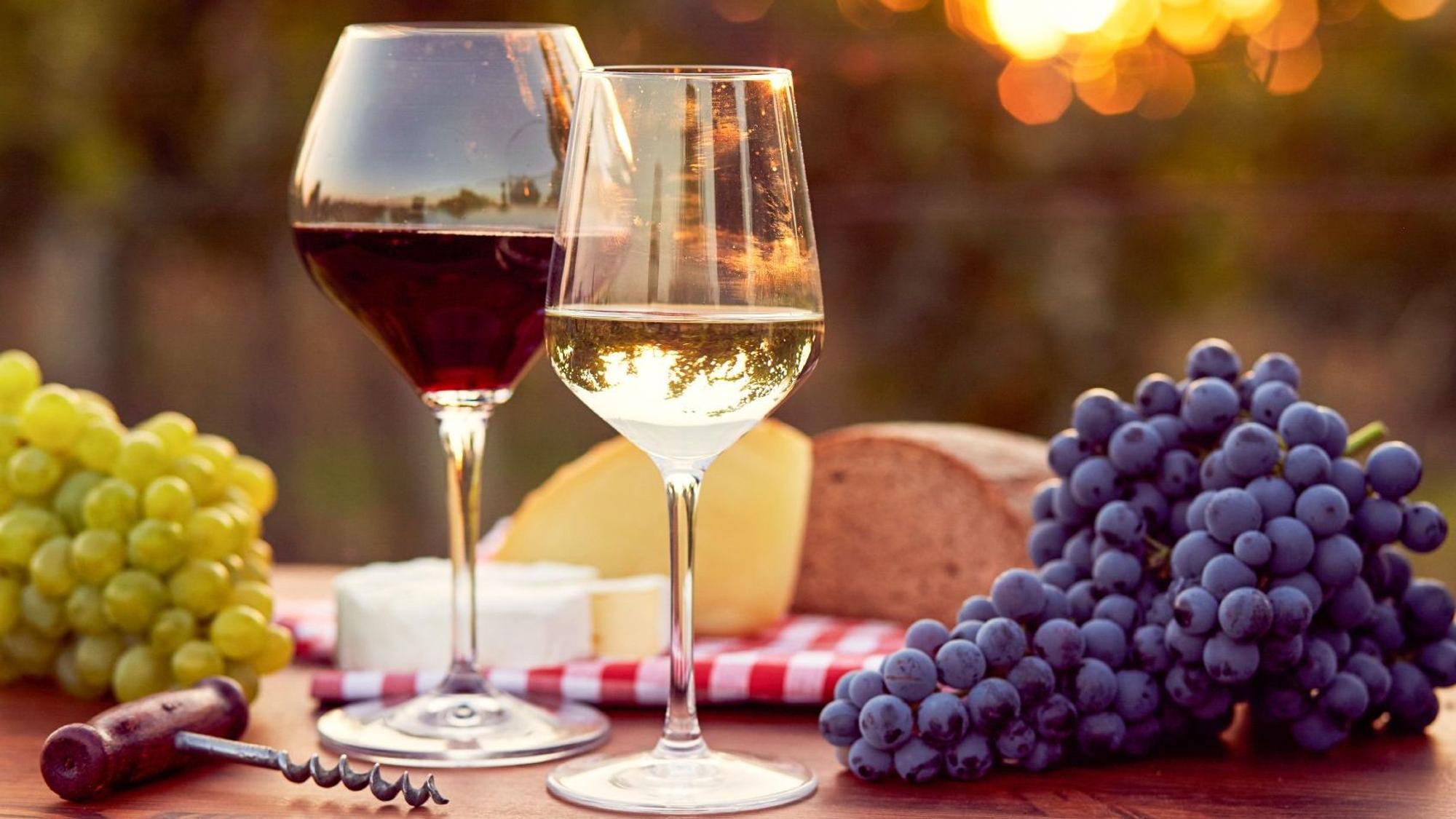 Ein Tisch mit zwei Gläsern Wein, Brot, Käse, Trauben und einem Korkenzieher.