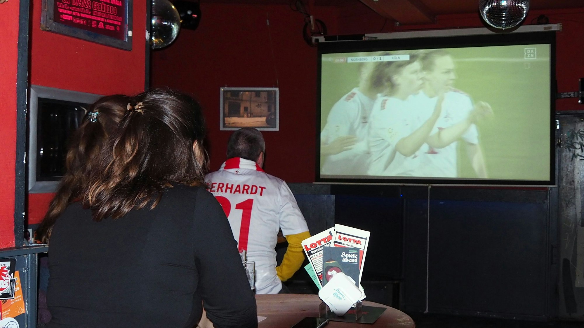 Eine Frau schaut auf einer Leinwand Fußball.