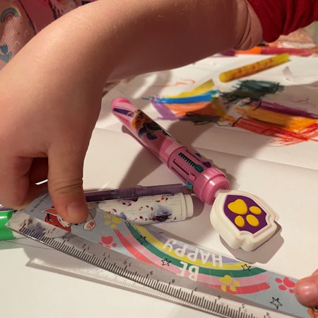 Das Bild zeigt die Hände eines Kita-Kindes, das ein Lineal in den Händen hält. Auch Stifte und Papier sind zu sehen.