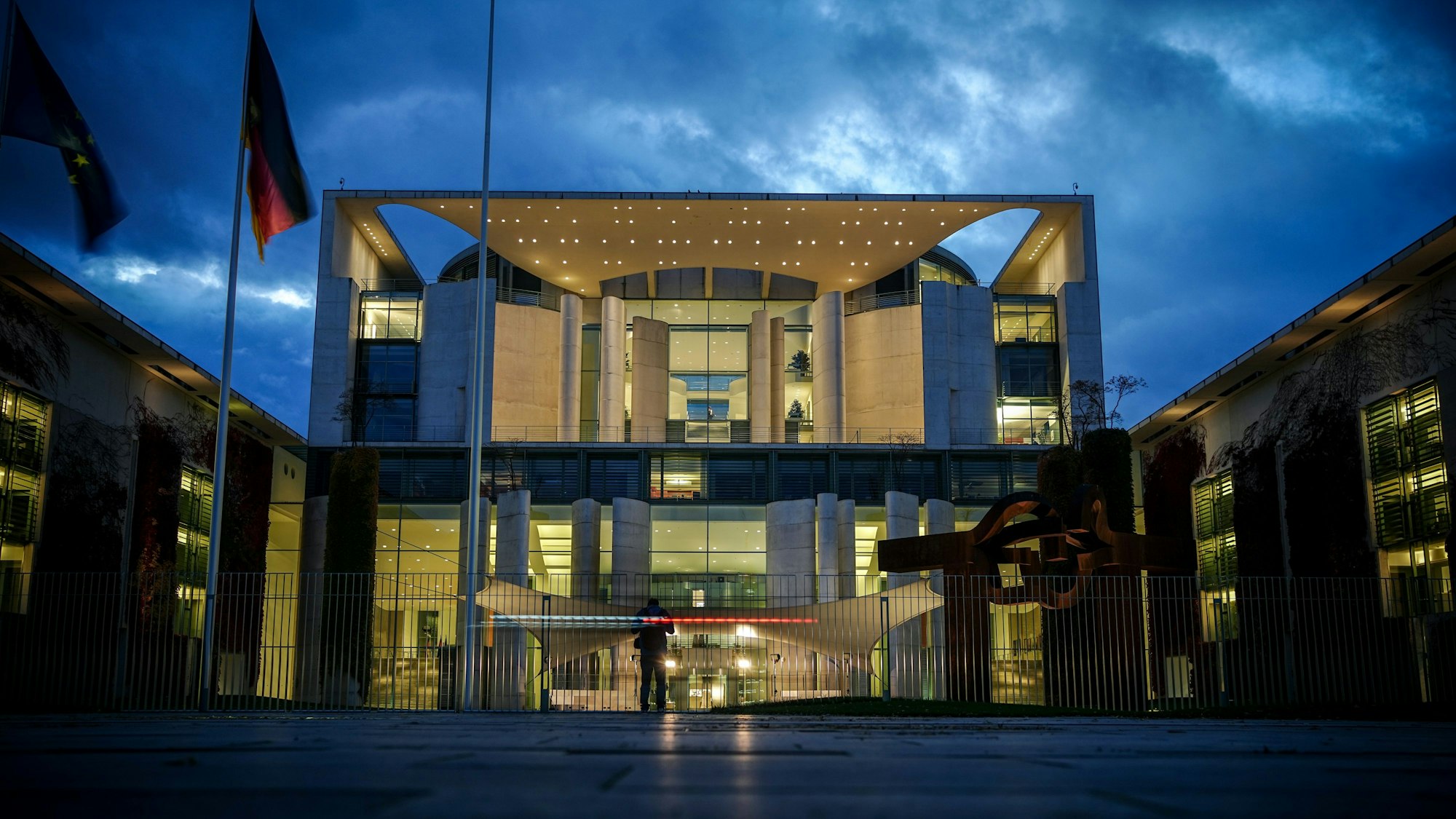 Das Bundeskanzleramt wird am Abend angestrahlt, vor ihm wehen eine Deutschland- und eine Europaflagge.