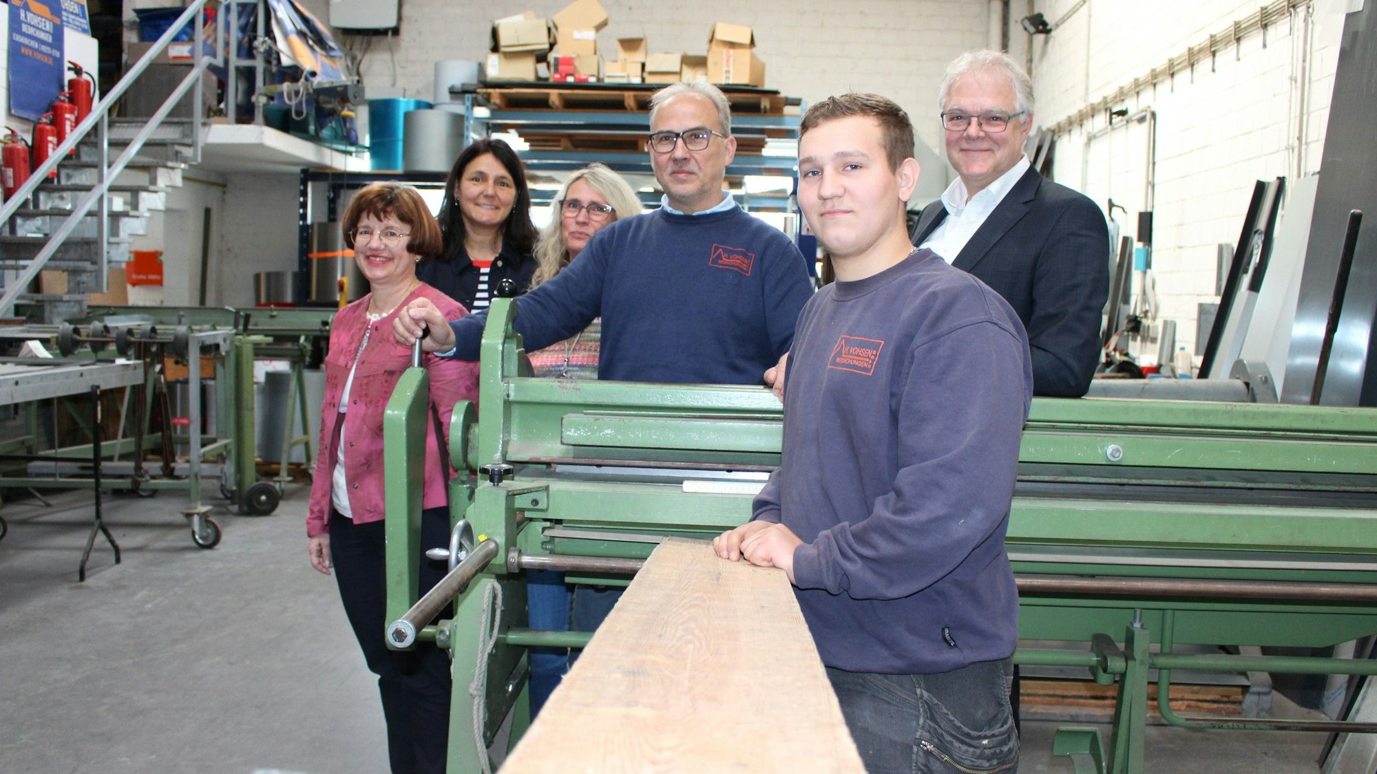 Das Bild zeigt Waltraud Gräfen (IHK), Anja Daub (Geschäftsführerin operativ der Agentur für Arbeit Brühl), Ruth und Dirk Schindler (Vohsen-Bedachungen), Azubi David Galkin und Ralf Holtkötter (Vorsitzender der Geschäftsführung der Agentur für Arbeit Brühl) in der Werkhalle der Firma Vohsen in Euskirchen.