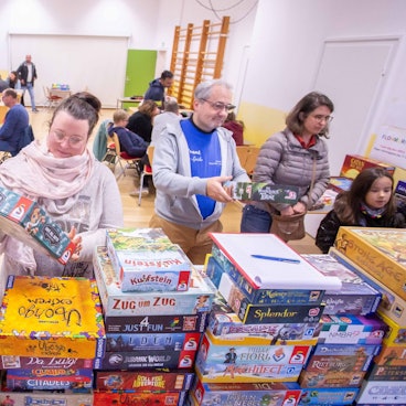 Das Foto zeigt Stabel mit Gesellschaftsspielen und Spieler im Hintergrund