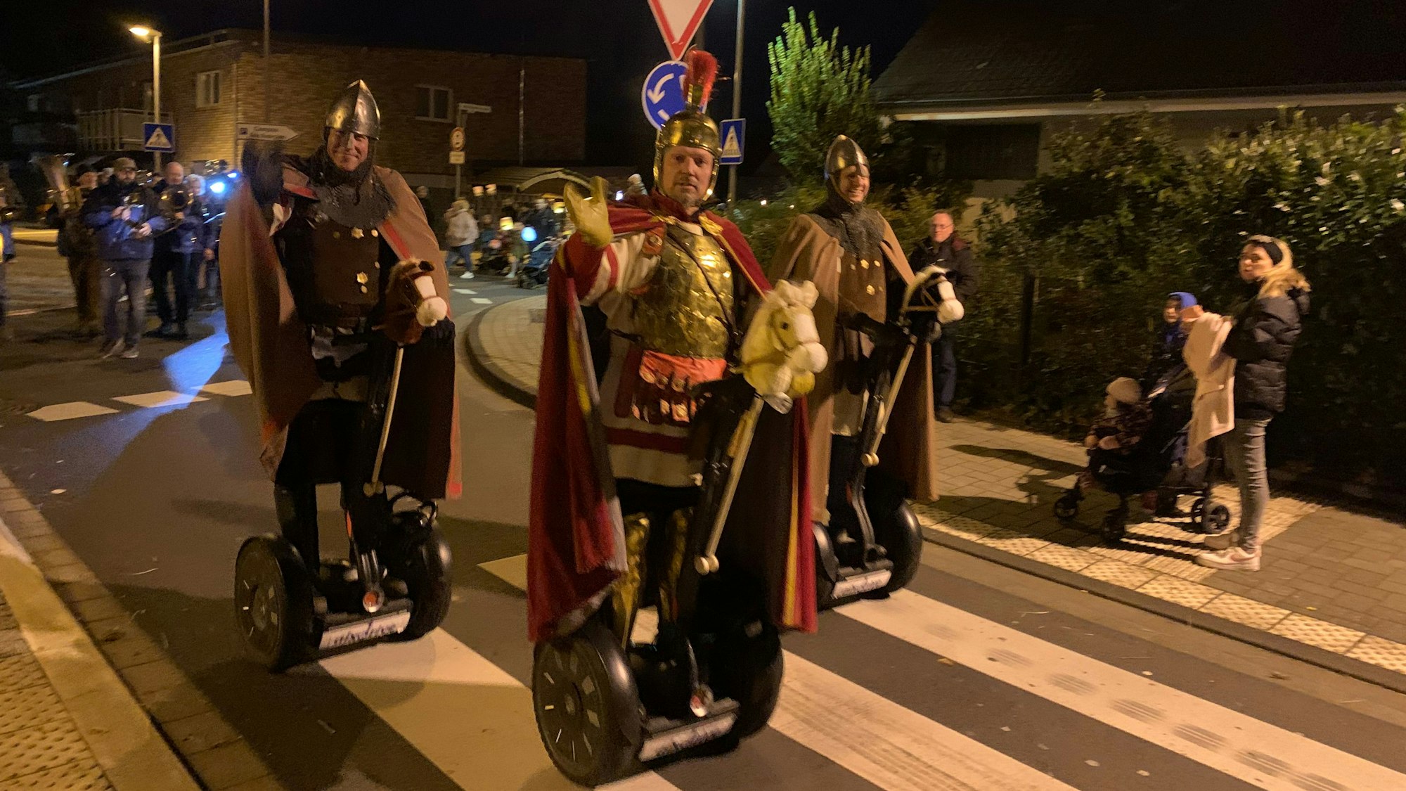 Drei Männer im Kostüm römischer Legionäre fahren auf Segway-Rollern über einen Zebrastreifen.