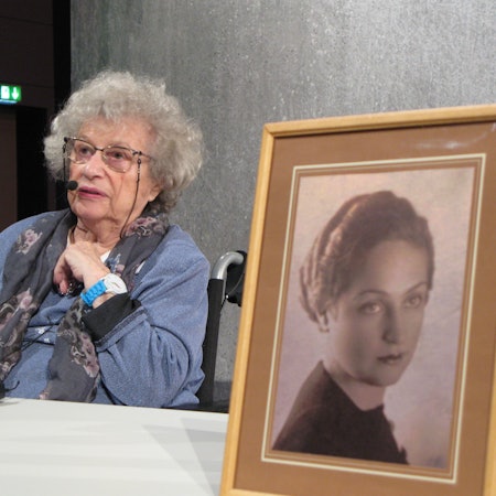 Tamar Dreifuss sitzt an einem Tisch, vorn steht eine gerahmte Fotografie ihrer Mutter.