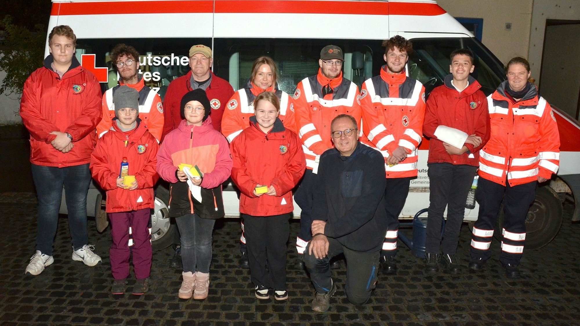 Gruppenbild mit den Mitgliedern des DRK-Ortsverbands Mechernich vor einem Rotkreuz-Kleinbus. Einige tragen Einsatzkleidung mit Reflektor-Streifen.