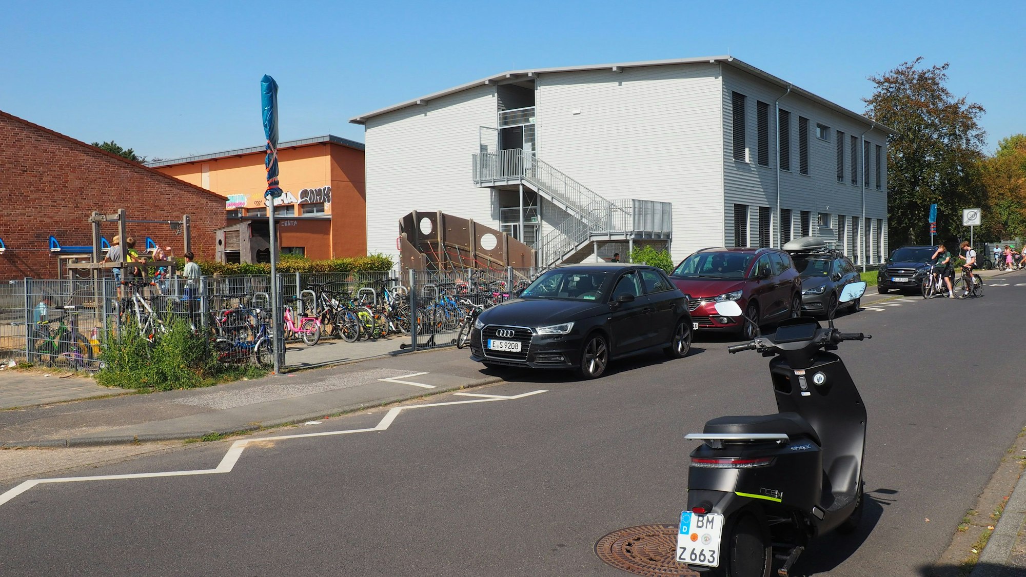 Im Hintergrund ist links ein Schulgebäude zu sehen, rechts ein Modulbau.