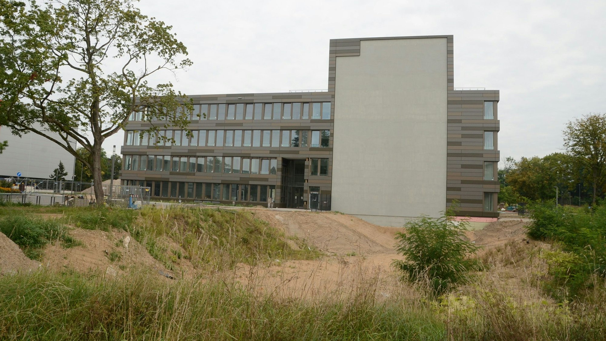 Ein modernes Bürogebäude mit vier Etagen; am Querbau markiert eine graue Fläche den geplanten Hotel-Anbau.