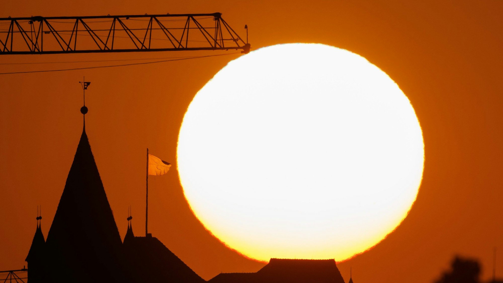 Die Sonne geht hinter der Kulisse der Kaiserburg und einem Baukran unter.