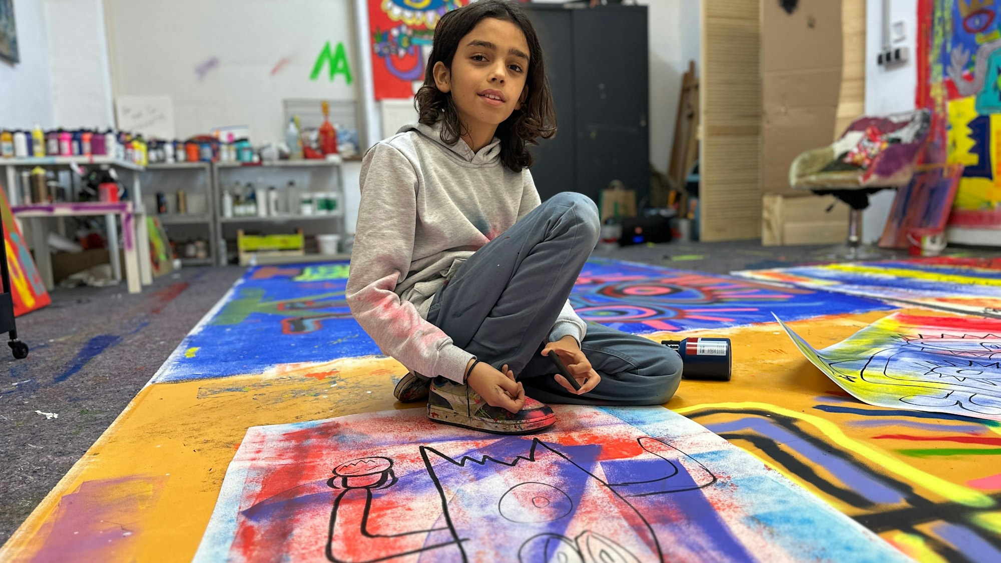 Ein Junge kniet auf einem farbenfrohen Bild mit abstrakten Form.